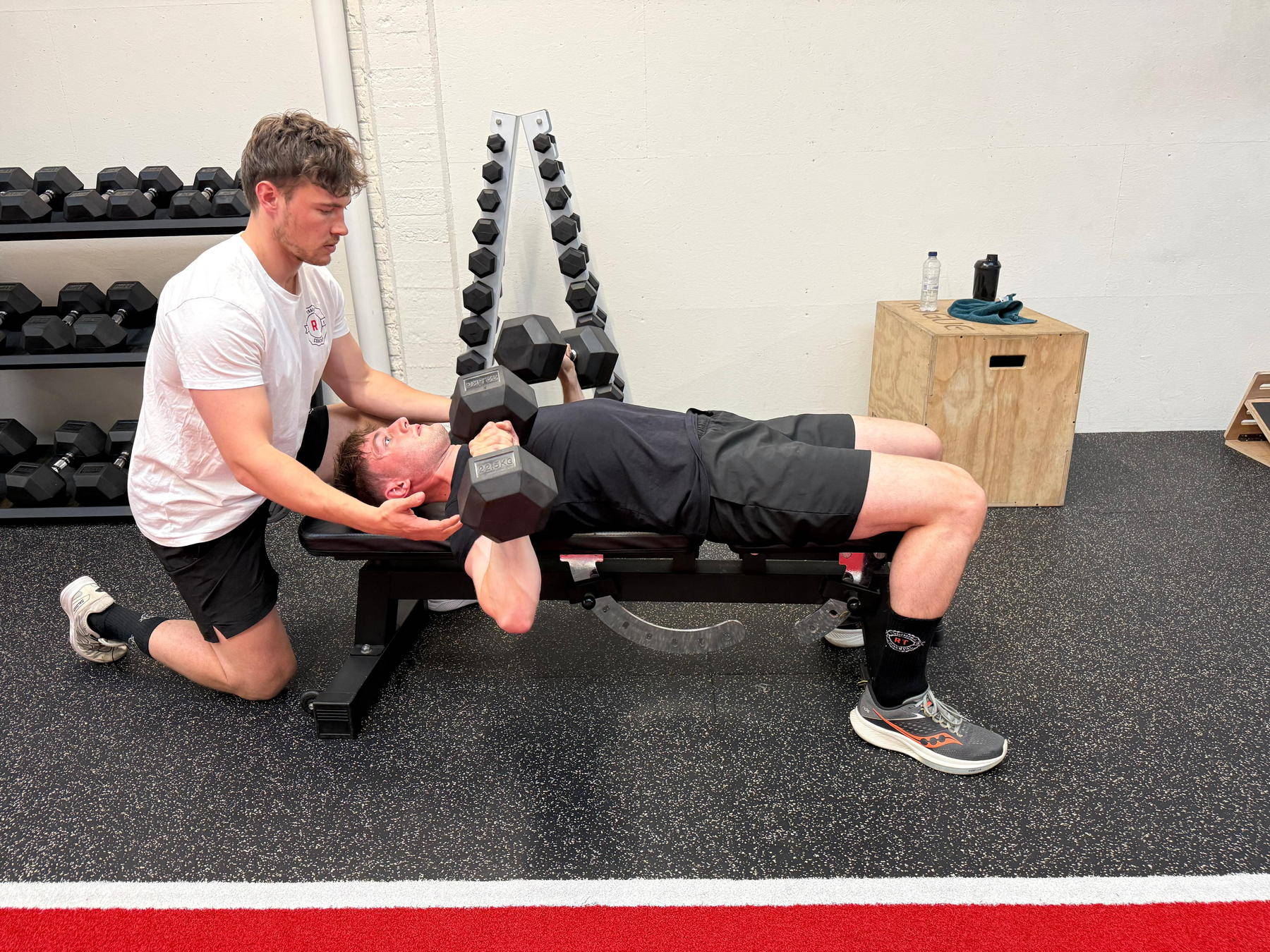Coach begeleidt dumbbell press tijdens personal training in Leuven